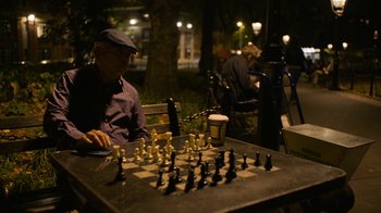 Movie still from “Full Circle” (2023), directed by Steven Soderbergh – An older man playing chess on a park bench at night; Wide shot, High angle