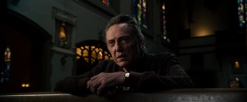 Movie still from “Stand Up Guys” (2012), directed by Fisher Stevens – A person sitting at a table in front of stained glass windows; Close Up shot, Low angle