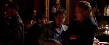 Movie still from “Stand Up Guys” (2012), directed by Fisher Stevens – A group of people gathered around a painting; Medium shot, Over the shoulder angle