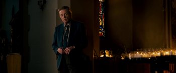 Movie still from “Stand Up Guys” (2012), directed by Fisher Stevens – A man in a suit and tie standing in front of a stained glass window; Medium shot, Low angle