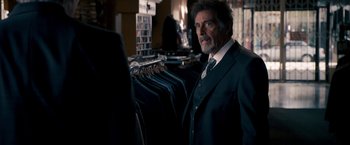 Movie still from “Stand Up Guys” (2012), directed by Fisher Stevens – A man wearing a suit and tie in a store; Medium shot, Over the shoulder angle