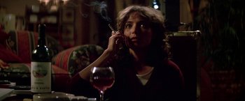 Movie still from “Starman” (1984), directed by John Carpenter – A woman sitting at a table smoking a cigarette and drinking wine; Close Up shot, Low angle