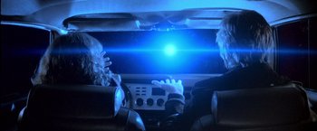 Movie still from “Starman” (1984), directed by John Carpenter – Two people sitting in a car in front of a blue light; Medium shot, Over the shoulder angle