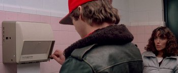 Movie still from “Starman” (1984), directed by John Carpenter – A man wearing a red hat looking at his cell phone; Close Up shot, Over the shoulder angle