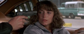 Movie still from “Starman” (1984), directed by John Carpenter – A person holding a gun in a car; Close Up shot, High angle
