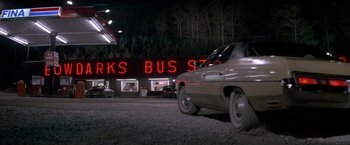 Movie still from “Starman” (1984), directed by John Carpenter – A car parked in a parking lot next to a bus stop at night; Extreme Wide shot, Low angle