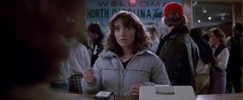 Movie still from “Starman” (1984), directed by John Carpenter – A young woman sitting at a table in front of a sign; Close Up shot, Over the shoulder angle