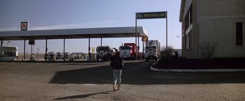 Movie still from “Starman” (1984), directed by John Carpenter – A woman is standing in a parking lot next to trucks; Wide shot, Low angle