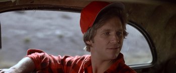 Movie still from “Starman” (1984), directed by John Carpenter – A man wearing a red hat sitting in the back of a car; Close Up shot, Over the shoulder angle