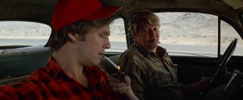 Movie still from “Starman” (1984), directed by John Carpenter – Two men sitting in the back seat of a car smoking; Close Up shot, Over the shoulder angle