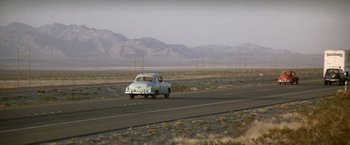 Movie still from “Starman” (1984), directed by John Carpenter – An old car is driving down the highway; Extreme Wide shot, High angle