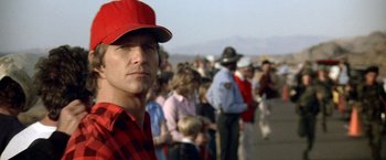 Movie still from “Starman” (1984), directed by John Carpenter – A man wearing a red hat standing in front of a group of people; Close Up shot, Low angle