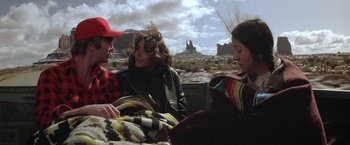 Movie still from “Starman” (1984), directed by John Carpenter – A group of people sitting in a vehicle on the side of the road; Wide shot, Over the shoulder angle