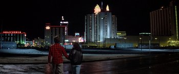Movie still from “Starman” (1984), directed by John Carpenter – A man and a woman holding hands in front of a city skyline at night; Wide shot, Low angle