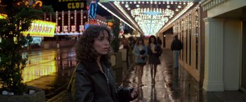 Movie still from “Starman” (1984), directed by John Carpenter – A woman is holding a cell phone while walking down the street; Medium shot, Over the shoulder angle