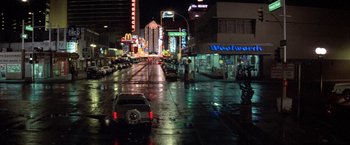Movie still from “Starman” (1984), directed by John Carpenter – A wet street at night with cars parked on the side of the road; Extreme Wide shot, High angle