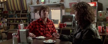 Movie still from “Starman” (1984), directed by John Carpenter – Two people sitting at a table with plates of food in front of them; Medium shot, Over the shoulder angle