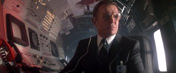 Movie still from “Starman” (1984), directed by John Carpenter – A man in a suit and tie wearing a headset; Medium shot, Low angle