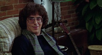 Movie still from “Stripes” (1981), directed by Ivan Reitman – A young man with curly brown hair wearing glasses and a plaid scarf; Close Up shot, Over the shoulder angle