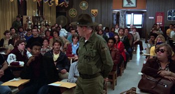 Movie still from “Stripes” (1981), directed by Ivan Reitman – A man in a military uniform standing in front of an audience; Medium shot, Over the shoulder angle