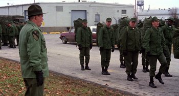 Movie still from “Stripes” (1981), directed by Ivan Reitman – A group of men in green jackets walking down a street; Wide shot, Over the shoulder angle