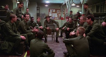 Movie still from “Stripes” (1981), directed by Ivan Reitman – A group of men sitting in a circle talking to each other; Wide shot, High angle