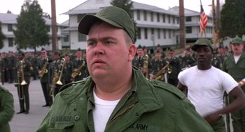 Movie still from “Stripes” (1981), directed by Ivan Reitman – A man in a green jacket and a green hat is in front of a group of soldiers; Close Up shot, Low angle