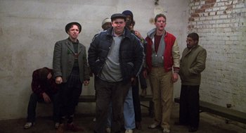 Movie still from “Stripes” (1981), directed by Ivan Reitman – A group of men standing next to each other in front of a wall; Wide shot, Low angle