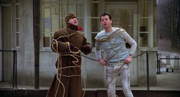 Movie still from “Stripes” (1981), directed by Ivan Reitman – Two men are tied up with ropes on a city street; Wide shot, High angle