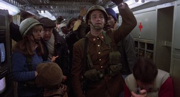 Movie still from “Stripes” (1981), directed by Ivan Reitman – A man dressed in a military uniform is standing in a crowded train; Medium shot, Low angle