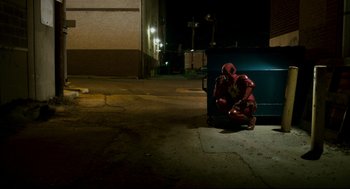 Movie still from “Super” (2010), directed by James Gunn – A man dressed as spider - man sitting next to a trash can; Wide shot, High angle