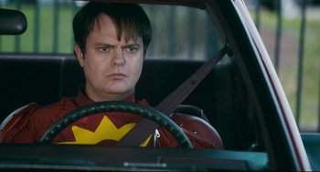 Movie still from “Super” (2010), directed by James Gunn – A man in a costume sitting in the drivers seat of a car; Close Up shot, Over the shoulder angle