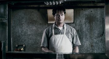 Movie still from “Super” (2010), directed by James Gunn – A man wearing an apron standing in front of a mirror; Close Up shot, Low angle