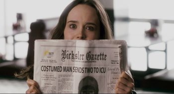Movie still from “Super” (2010), directed by James Gunn – A woman holding up a news paper with a gorilla on it's face; Close Up shot, Over the shoulder angle