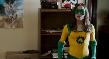 Movie still from “Super” (2010), directed by James Gunn – A woman dressed as a superhero poses in front of a book shelf; Medium shot, Low angle