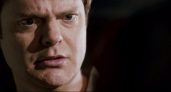 Movie still from “Super” (2010), directed by James Gunn – A man's face in a dark room; Close Up shot, Over the shoulder angle