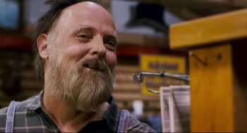 Movie still from “Super” (2010), directed by James Gunn – A man with a long beard is smiling for the camera; Close Up shot, Over the shoulder angle