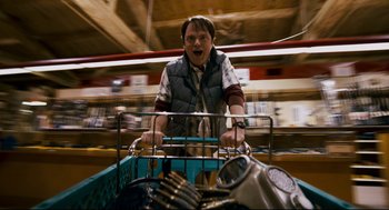 Movie still from “Super” (2010), directed by James Gunn – A man riding on the back of a shopping cart; Medium shot, High angle