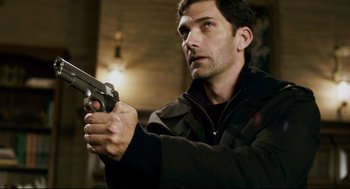 Movie still from “Super” (2010), directed by James Gunn – A man holding a gun while wearing a black jacket; Close Up shot, High angle