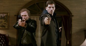 Movie still from “Super” (2010), directed by James Gunn – Two men are holding guns and aiming at the camera; Medium shot, Low angle
