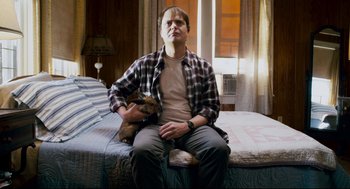 Movie still from “Super” (2010), directed by James Gunn – A man sitting on top of a bed holding a dog; Medium shot, Low angle