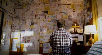 Movie still from “Super” (2010), directed by James Gunn – A man standing in front of a wall covered with papers; Wide shot, Over the shoulder angle