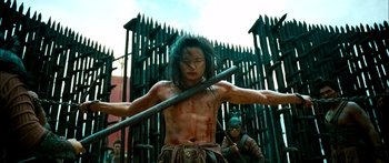 Movie still from “Ong Bak 3” (2010), directed by Tony Jaa – A man holding a wooden stick in his hands; Medium shot, Low angle