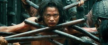 Movie still from “Ong Bak 3” (2010), directed by Tony Jaa – A man is holding a bunch of wooden sticks; Medium shot, Low angle