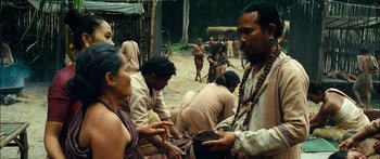 Movie still from “Ong Bak 3” (2010), directed by Tony Jaa – A group of people sitting on a dirt road; Medium shot, Over the shoulder angle