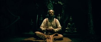 Movie still from “Ong Bak 3” (2010), directed by Tony Jaa – A man sitting on the ground with his eyes closed; Wide shot, Low angle