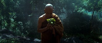 Movie still from “Ong Bak 3” (2010), directed by Tony Jaa – A man in a robe holding a plant in front of a forest; Medium shot, Low angle