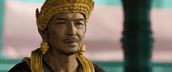 Movie still from “Ong Bak 3” (2010), directed by Tony Jaa – A person wearing a gold crown; Close Up shot, Over the shoulder angle