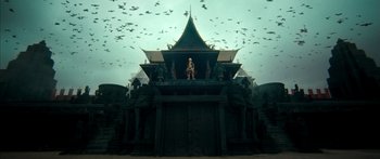 Movie still from “Ong Bak 3” (2010), directed by Tony Jaa – A statue of a person on top of a building with birds flying overhead; Extreme Wide shot, Low angle