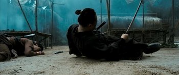 Movie still from “Ong Bak 3” (2010), directed by Tony Jaa – A person laying on the ground holding a gun; Wide shot, High angle